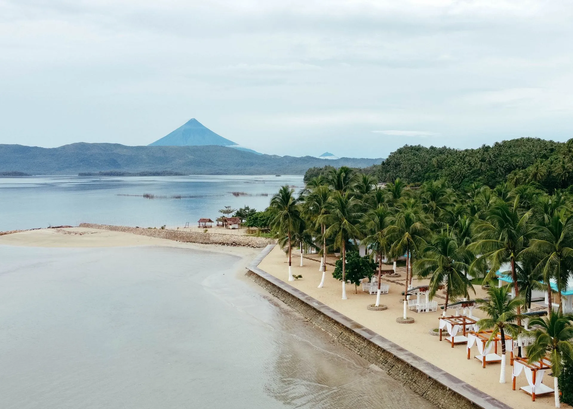 Palm-lined beach with draped cabanas facing a calm bay